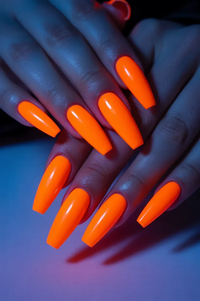 Bright neon orange coffin nails glowing under UV light